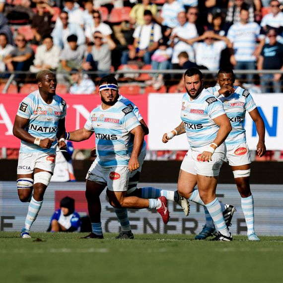 Joueurs du Racing 92 en plein match de rugby, portant leur maillot bleu et blanc à rayures, sous les yeux des spectateurs en tribune.