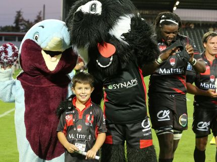 Un jeune supporter pose avec les joueurs et les mascottes du LOU Rugby.